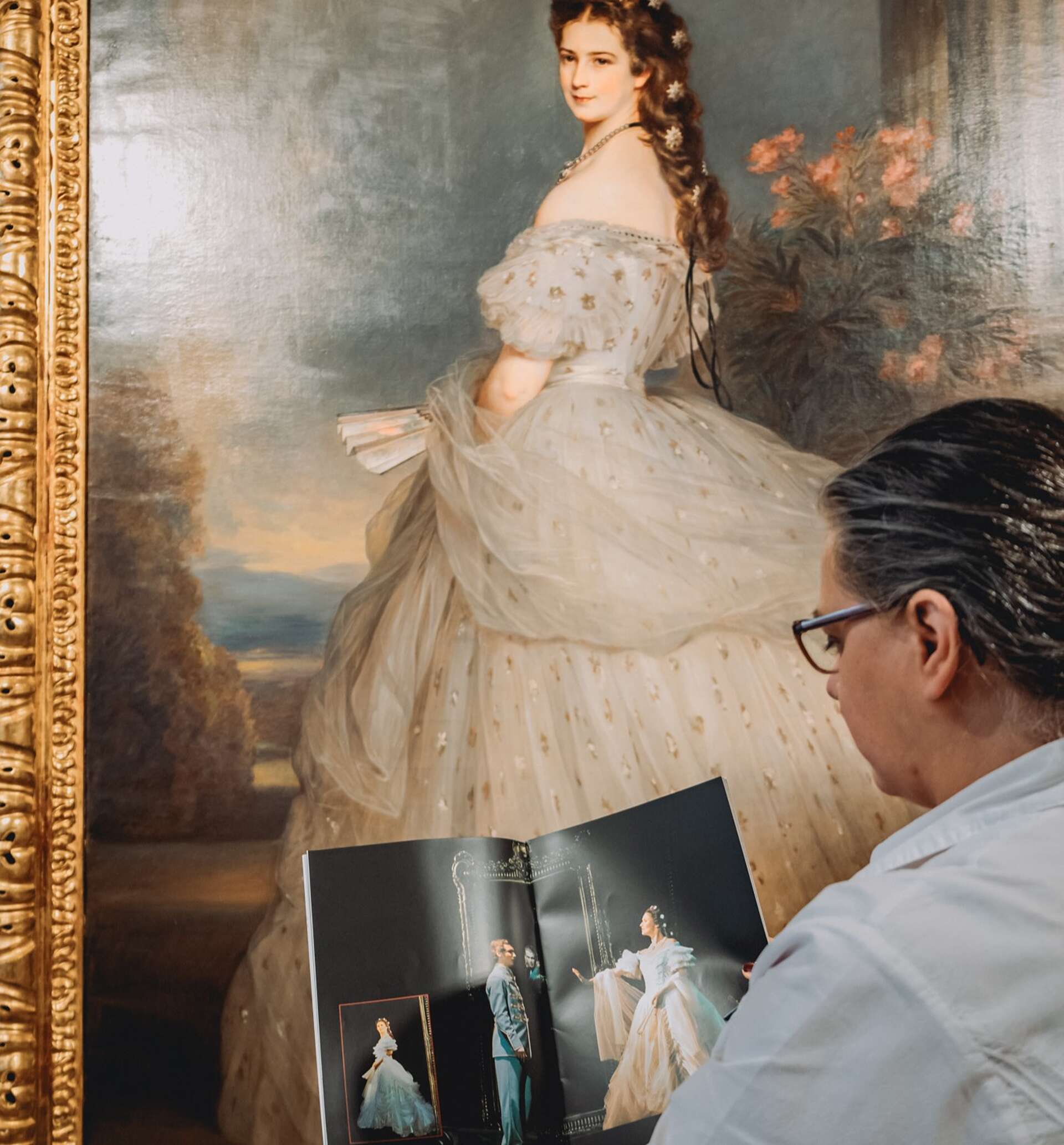 Mitarbeiterin liest sich das Elisabeth Musical Programm durch, während sie vor einem Portrait von Kaiserin Elisabeth steht